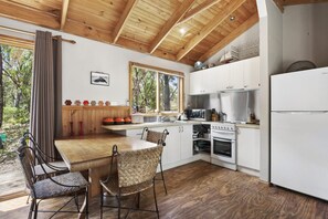Eine moderne Küche mit weißen Schränken, einer Holzbalkendecke und einem Essbereich mit Korbstühlen.