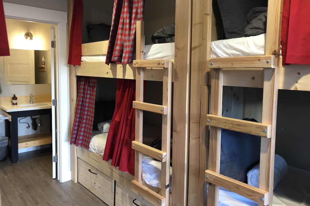 A bunk bed room with a wooden frame, a small desk with a mirror, and a sink.