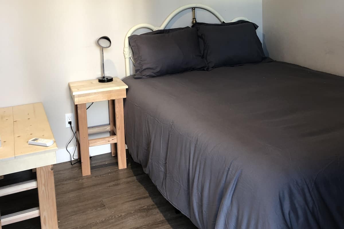 A bedroom with a bed, a bedside table with a lamp, and a wooden desk.