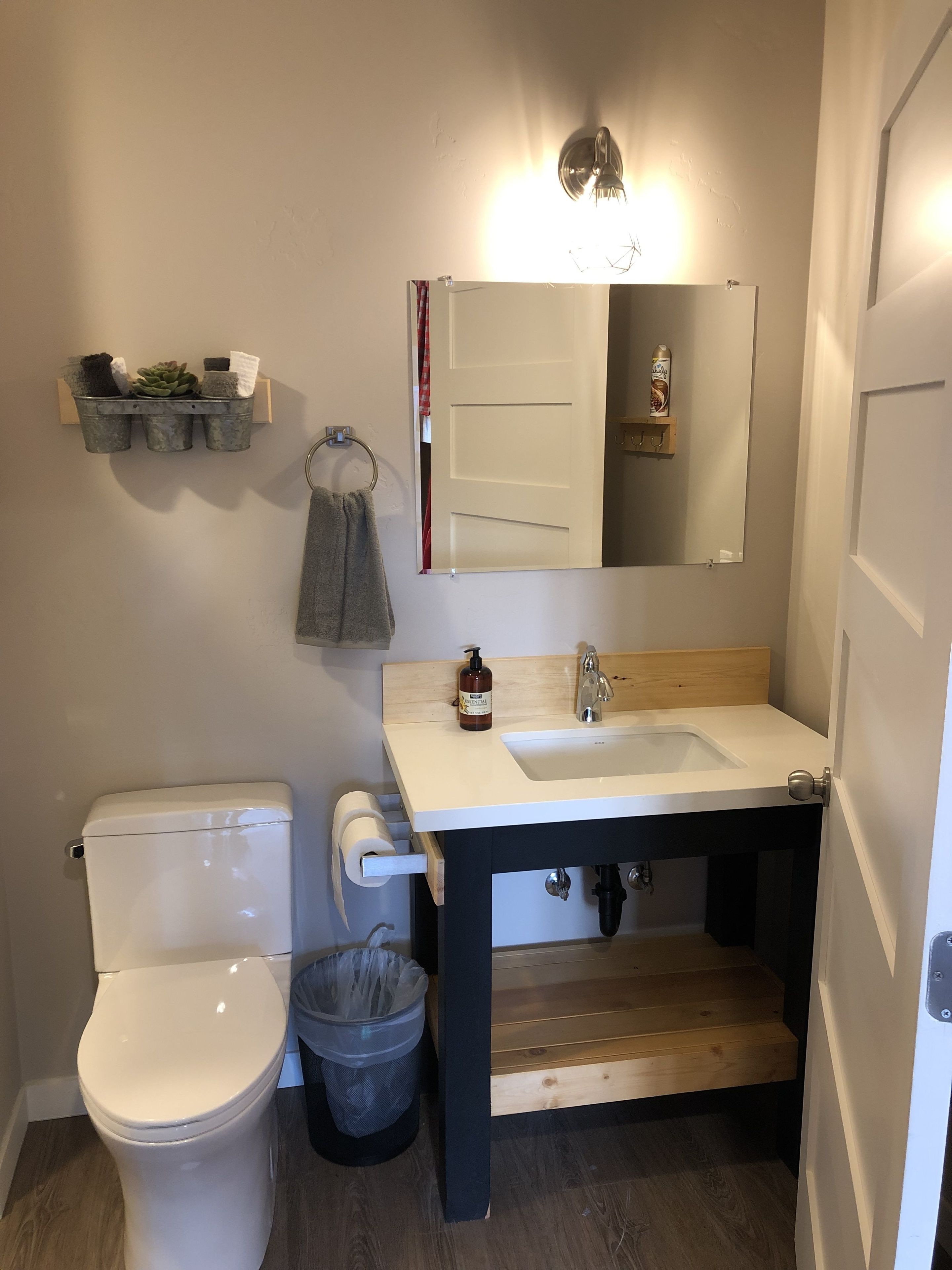 Une salle de bain avec des toilettes blanches, un meuble-lavabo en bois avec un évier, un miroir et un espace douche.