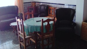 Ein Essbereich mit einem runden Tisch, Stühlen und einer Chandelier. An den Wänden hängen Bilder in Rahmen, und ein Fliesenstreifen verläuft entlang des Bodens.