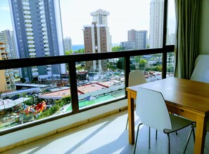 Ein Zimmer mit großem Fenster und Blick auf eine Stadtlandschaft, einem Esstisch und einem Stuhl.