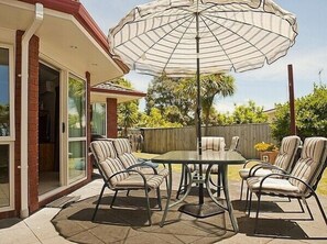A patio with a table and chairs, an umbrella, and a view of a house.