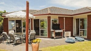 A house with a patio, outdoor seating, a barbecue, and a large window.