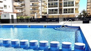 A swimming pool with clear blue water, surrounded by a black fence, and adjacent to a multi-story residential building. - APARTBEACH ADRIATICO RELAX BEACHFRONT WITH SWIMMING POOL AND PARKING (La Pineda)
