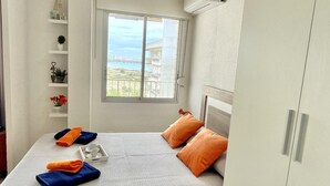 A bedroom with a bed, a window with a view, a shelf with decorative items, and a tray with towels and cups. - APARTBEACH ADRIATICO RELAX BEACHFRONT WITH SWIMMING POOL AND PARKING (La Pineda)