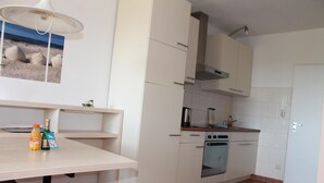A kitchen with white cabinets, a stove, and a sink. There are two bottles on the counter. - Apartment E623 for 2-4 people on the Baltic Sea (Schönberg OT Holm)