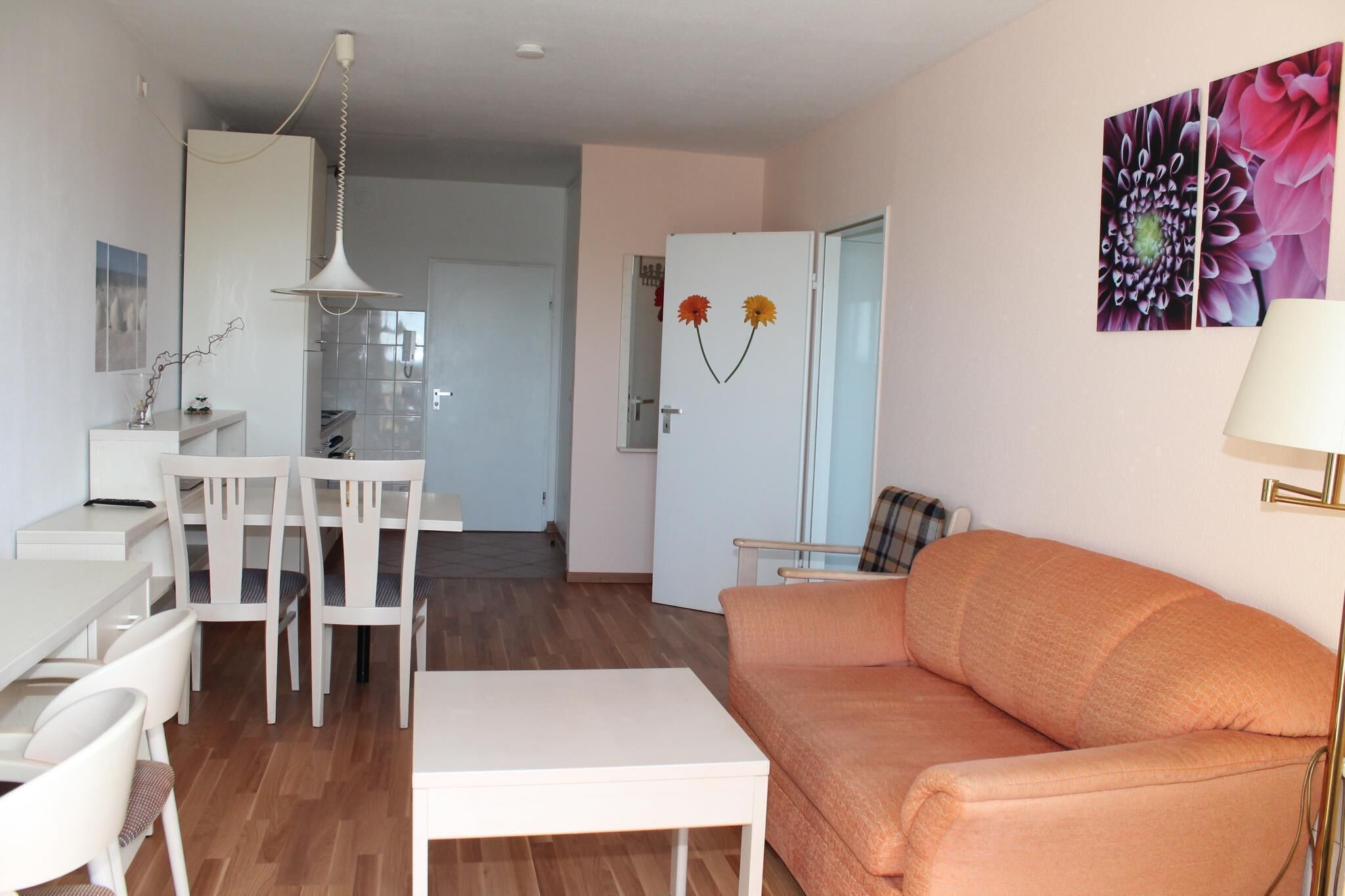 A modern living room with a white dining area, a sofa, and a kitchen in the background.