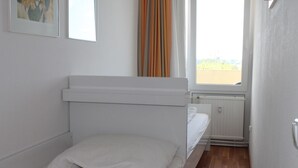 A small, clean room with a single bed, a window with curtains, and a radiator. - Apartment E623 for 2-4 people on the Baltic Sea (Schönberg OT Holm)