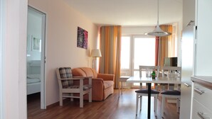 A modern living room with a sofa, a dining table with chairs, a TV, and a lamp. - Apartment E623 for 2-4 people on the Baltic Sea (Schönberg OT Holm)