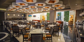 Een ruime restaurantruimte met meerdere eettafels en stoelen, een bar en een modern plafondontwerp.