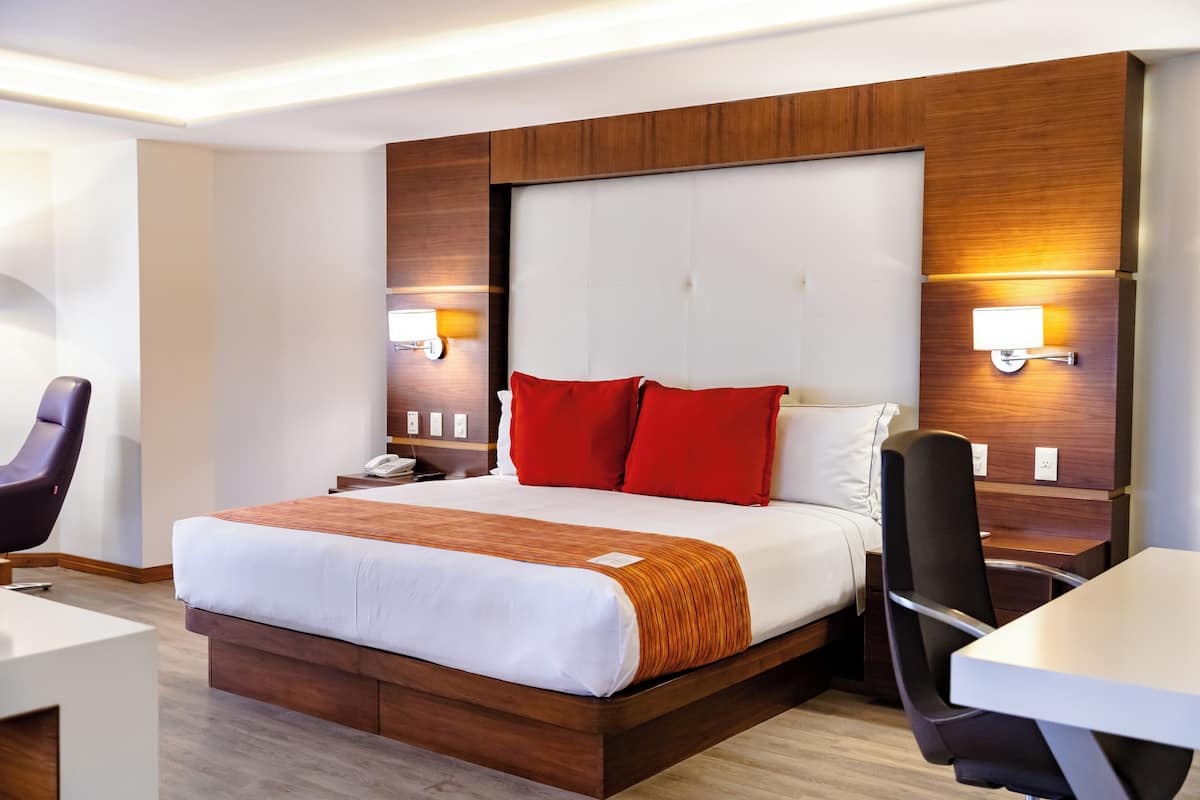 A modern hotel room with a large bed, a desk, and two chairs.