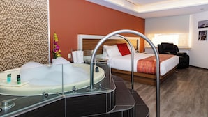 A hotel room with a large bathtub, a bed with a red pillow, a chair, and a wall with a patterned design. - JF Grand Puebla (Puebla)