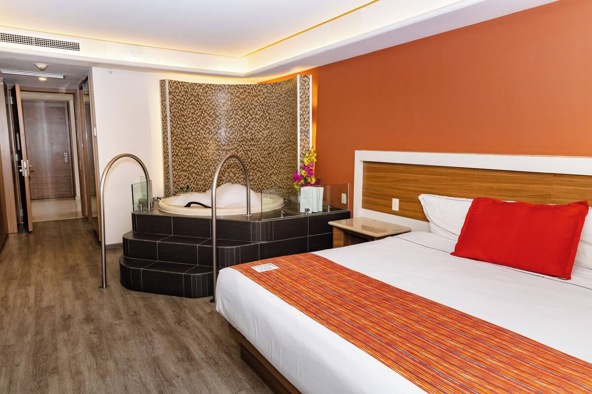 A hotel room with a large bed, a bathroom with a bathtub, and a wooden floor.