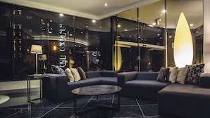 A modern hotel lobby with a dark-colored sofa set, a round coffee table, and a large floor lamp. - JF Grand Puebla (Puebla)