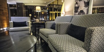 Un área de descanso moderna con sofás y sillones estampados, una pequeña mesa redonda e iluminación ambiental.