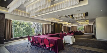 Een congreszaal met lange tafels en stoelen, grote ramen en een kroonluchter.