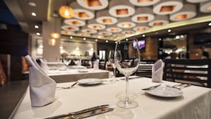 A dining table set with a wine glass, plates, and cutlery in a restaurant with a modern ceiling design. - JF Grand Puebla (Puebla)