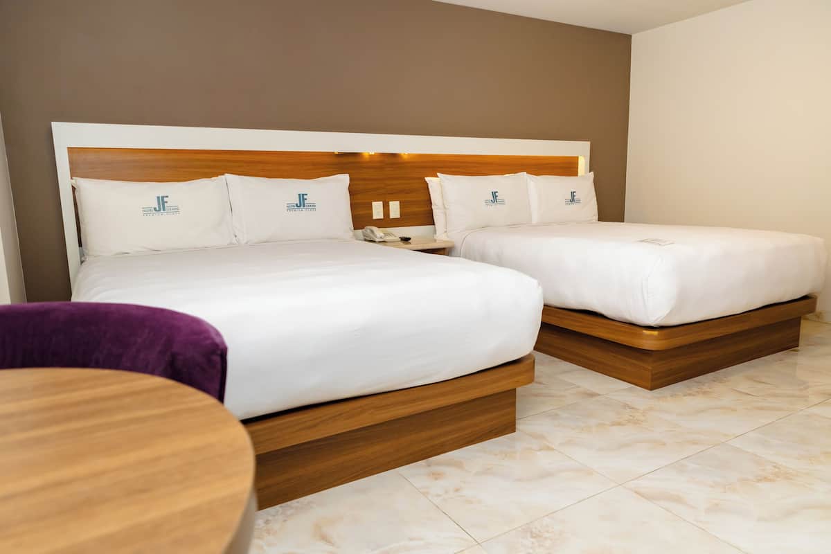 A hotel room with two beds, a wooden headboard, and a round wooden table.