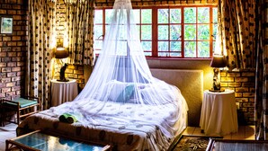 A room with a bed under a canopy, a table, a chair, and a view of greenery through the window. - Masasana's Rest (Mbombela)