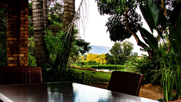 A dining area with a table and chairs, surrounded by lush greenery and a view of a landscape with trees and a body of water. - Masasana's Rest (Mbombela)