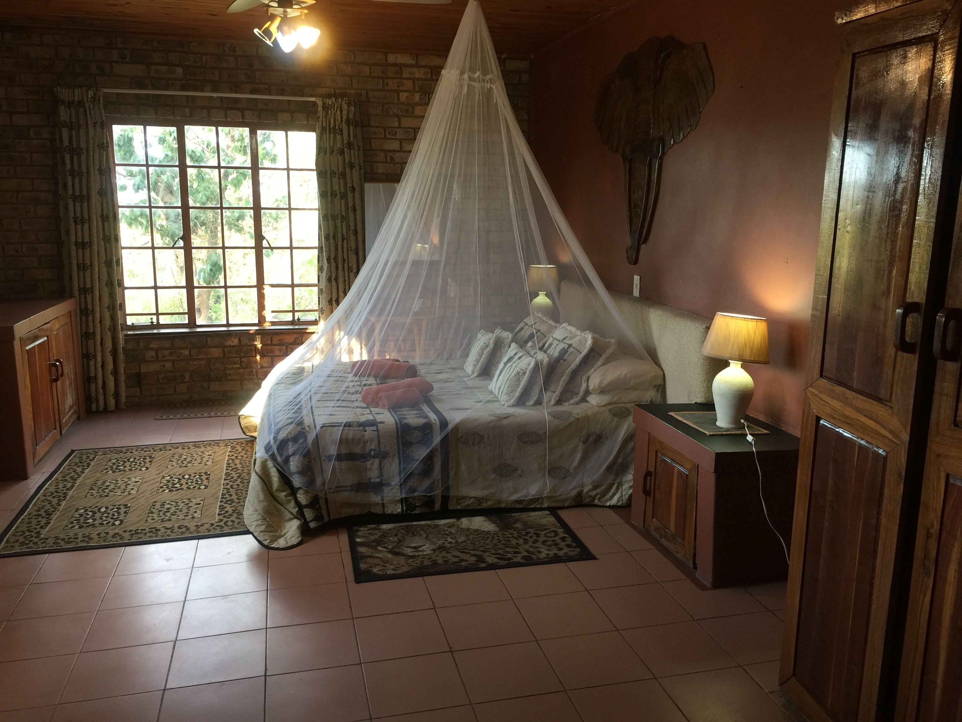 Une chambre à coucher avec un lit recouvert d’une moustiquaire, une table de chevet avec une lampe, une armoire en bois et une fenêtre avec des rideaux.