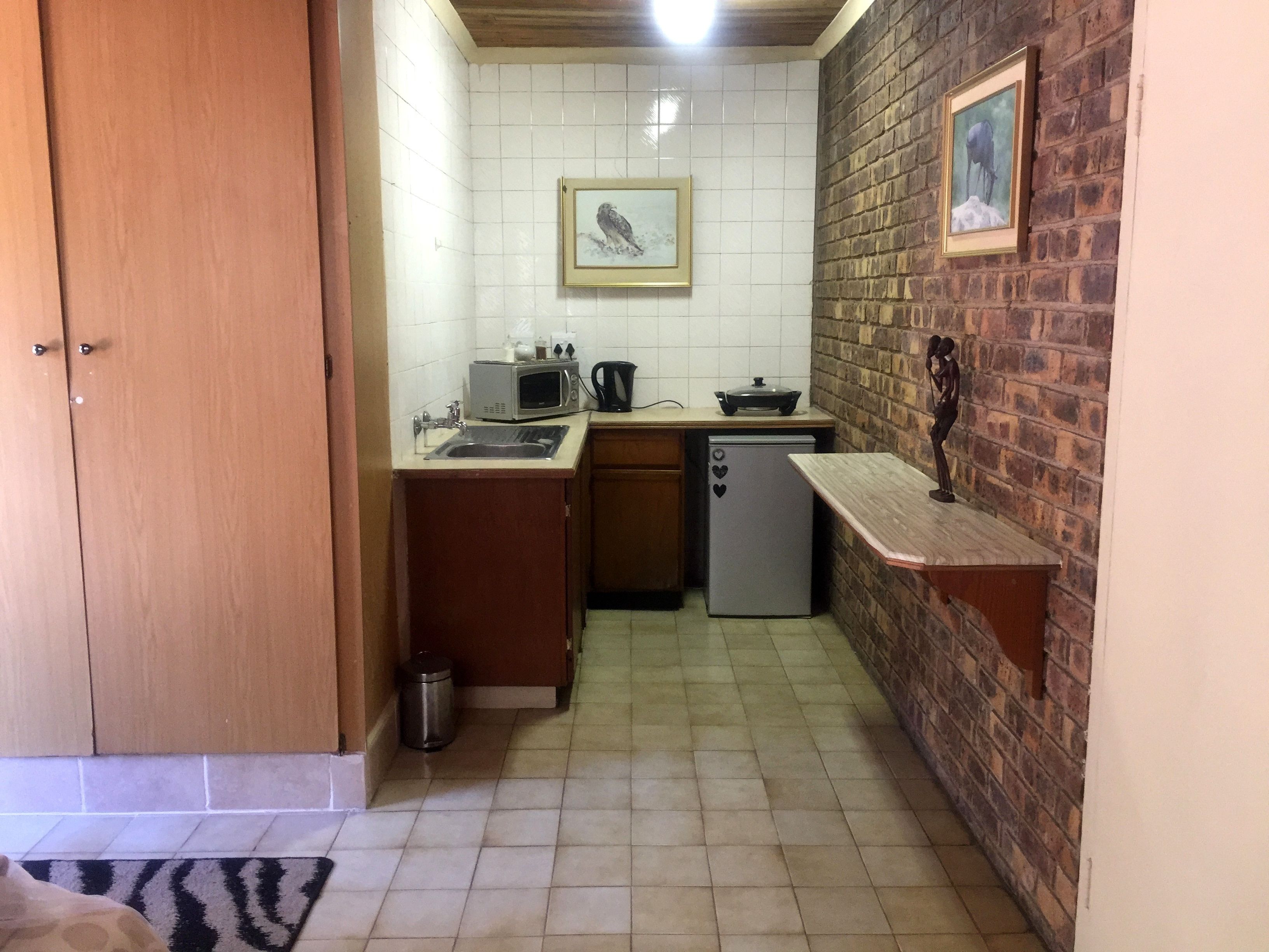 Una cocina compacta con paredes de azulejos blancos, una puerta de madera, un refrigerador pequeño y un lavabo.