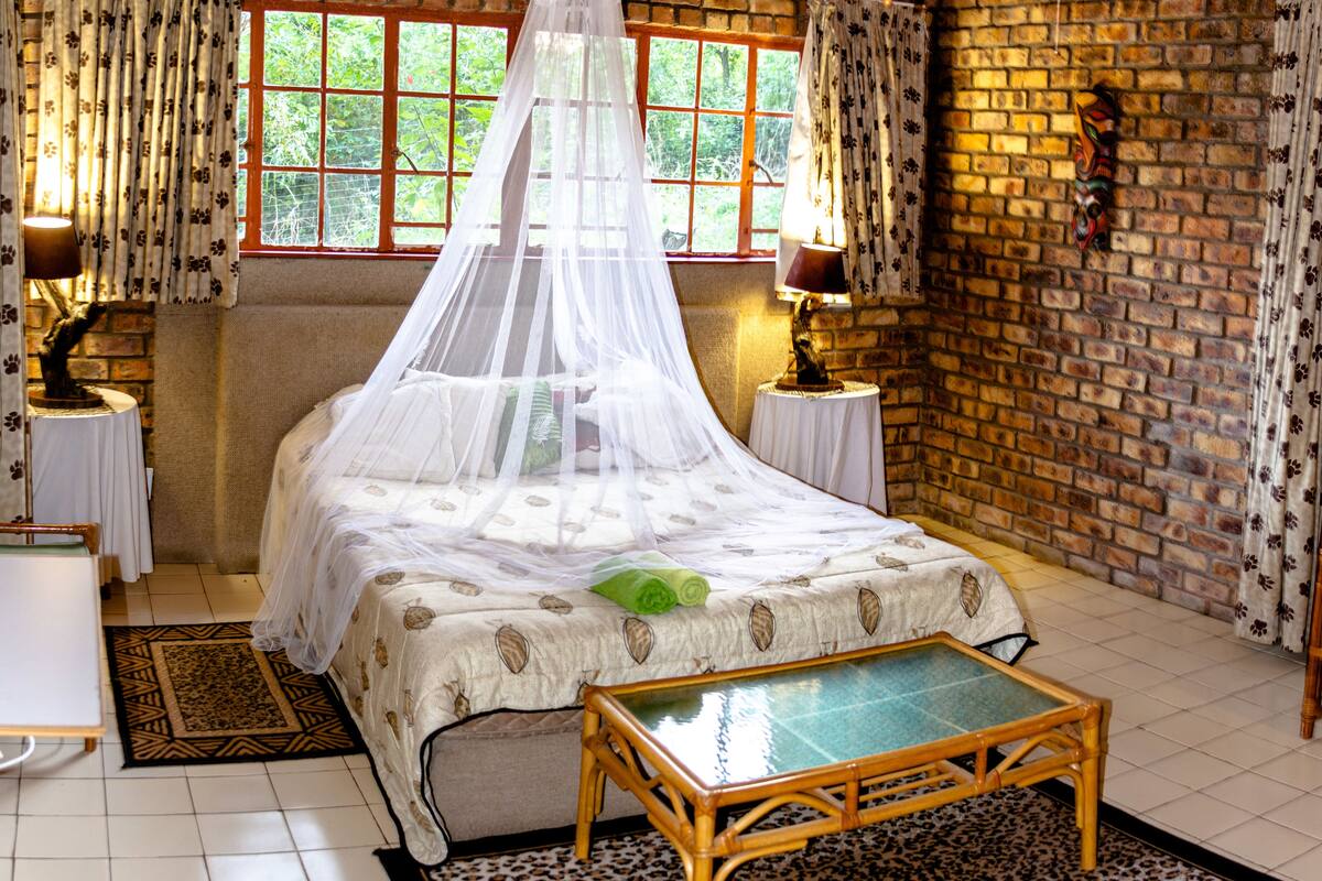 Una habitación con una cama, una mesita, una lámpara y una pared de ladrillo.