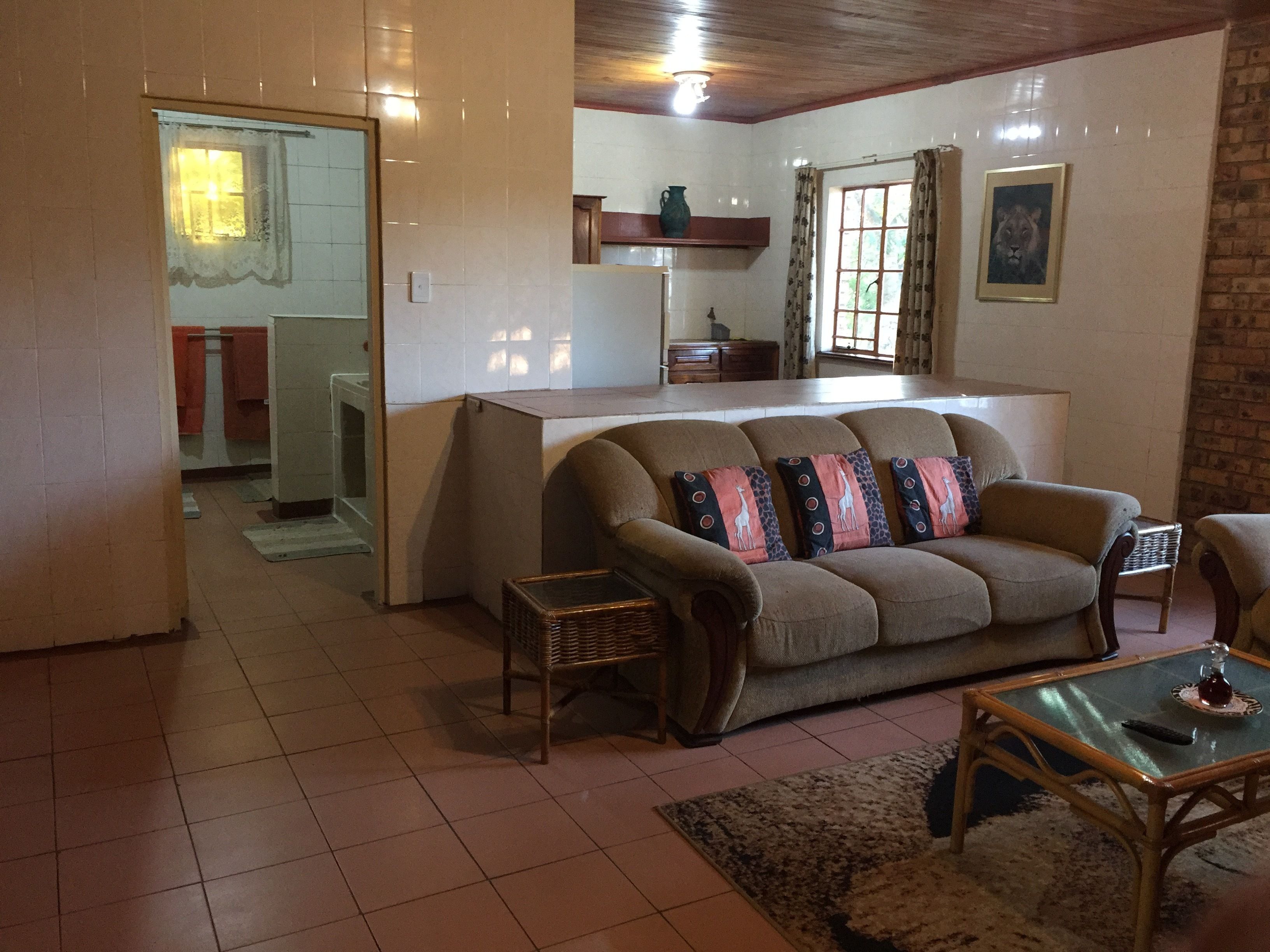 Un salón con sofá, mesa de centro y una mesita auxiliar. Se observa una cocina al fondo, con ventana y puerta que da a otra habitación.