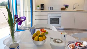 Une cuisine moderne avec des meubles blancs, un four encastré et un évier. On peut voir un bol de citrons et un vase avec des fleurs violettes sur la table.