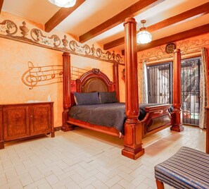 Ein Schlafzimmer mit einem Himmelbett, einem Holzschrank, einem Fernseher und einem gemusterten Sessel.
