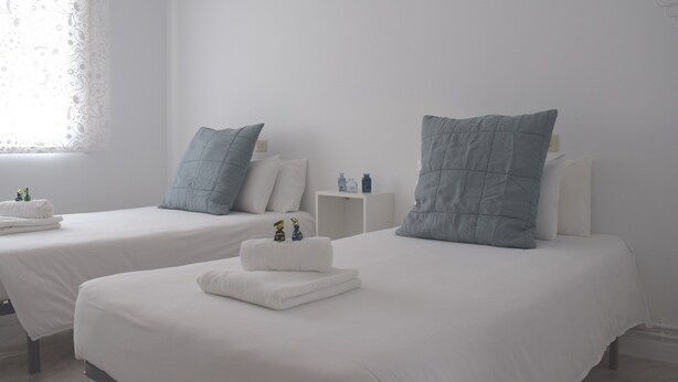 Een hotelkamer met twee bedden, elk met een witte matras en een blauw kussen. Op elk nachtkastje staan kleine flesjes en een decoratief object.