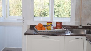 Een keuken met witte kastjes, een roestvrijstalen spoelbak en een raam met uitzicht op groen.