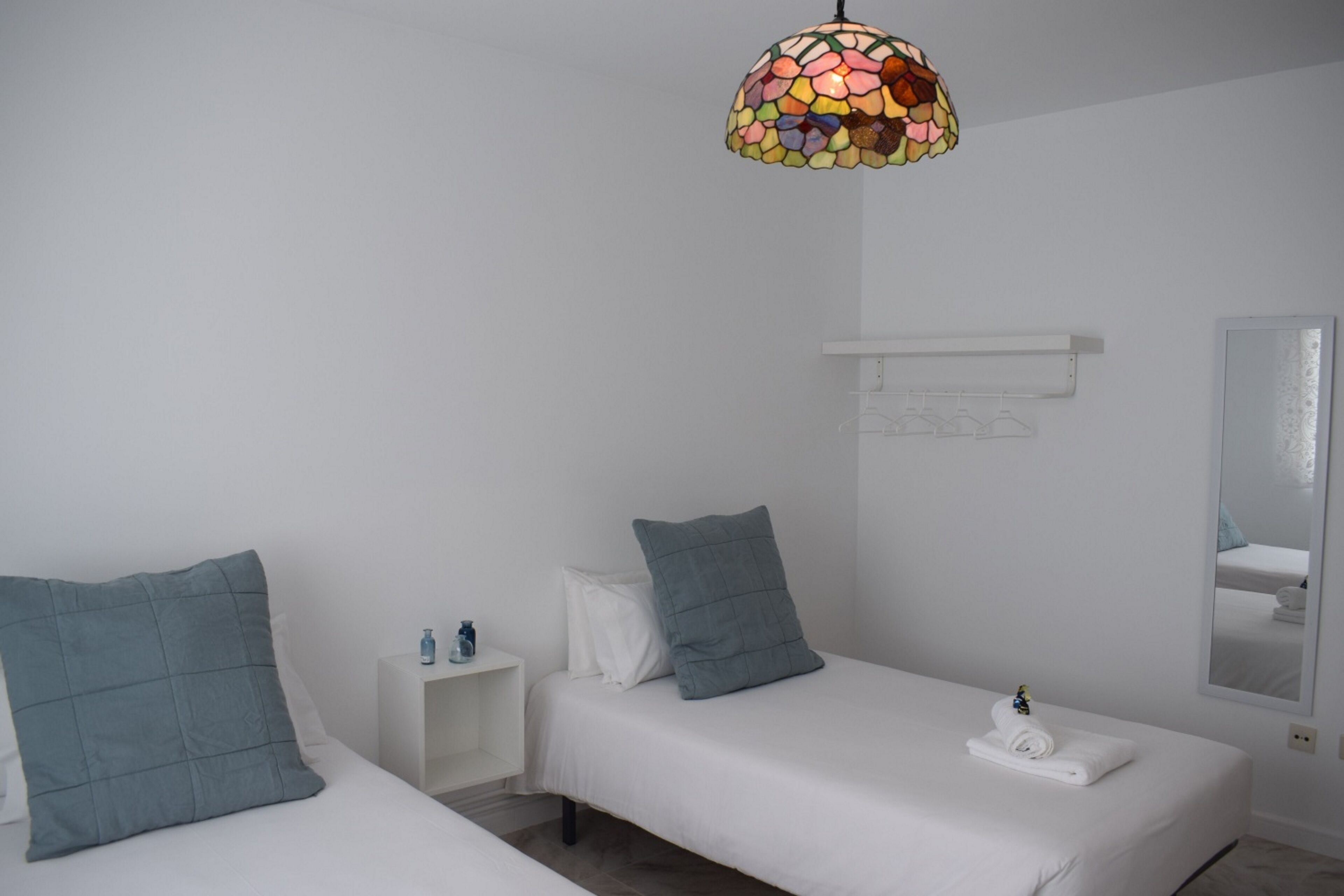 Une chambre avec deux lits, une table de chevet, un miroir et un luminaire suspendu aux couleurs vives.