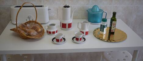 A kitchen counter with a toaster, coffee maker, and a blue juicer. There are also two bottles of olive oil and a basket of bread.