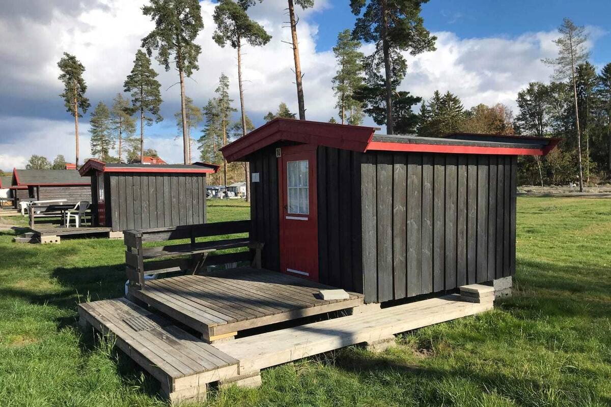 A small wooden cabin with a red door and a red roof, situated on a grassy field with a picnic table nearby.