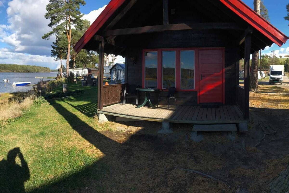 A cabin with a wooden deck, a covered outdoor seating area, and a view of a lake.