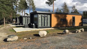 A modern cabin with a wooden exterior and large windows, situated in a forested area with a gravel path and rocks in front. - O'Lin Lake Resort (Hole)