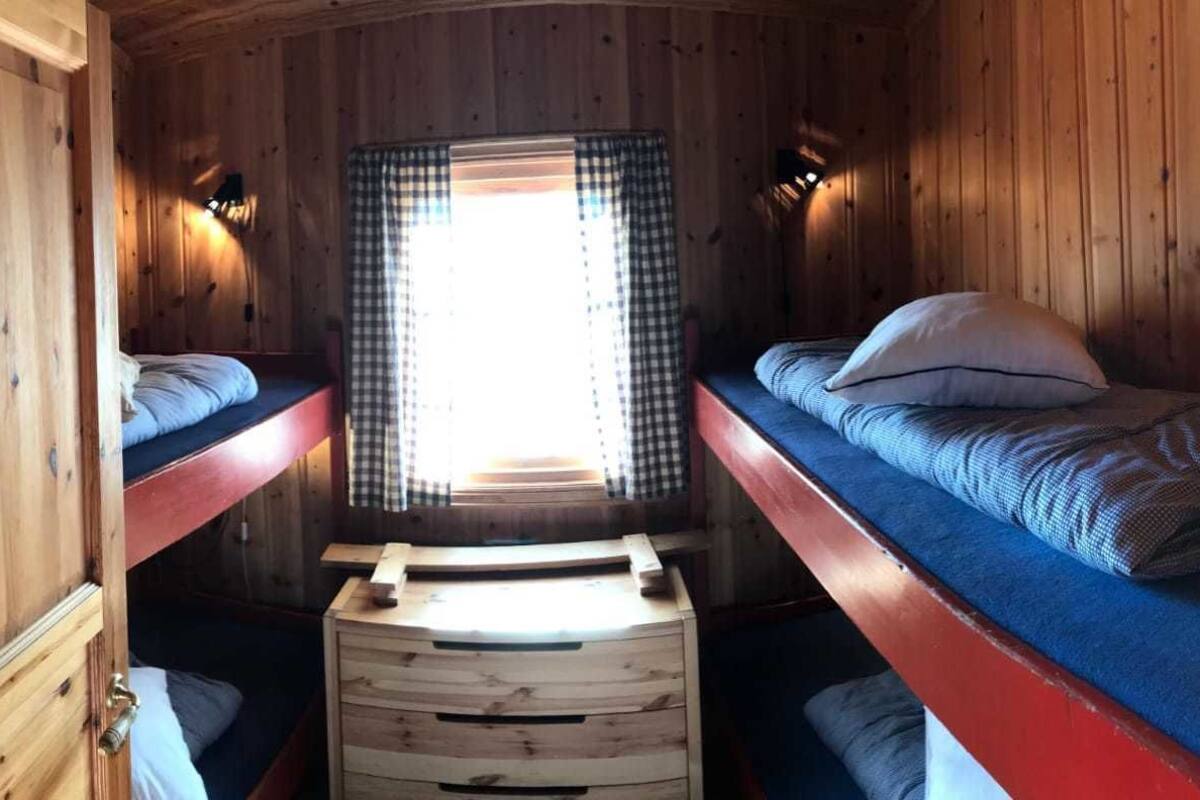 A cabin interior with two bunk beds, a window with checkered curtains, and a wooden cabinet.