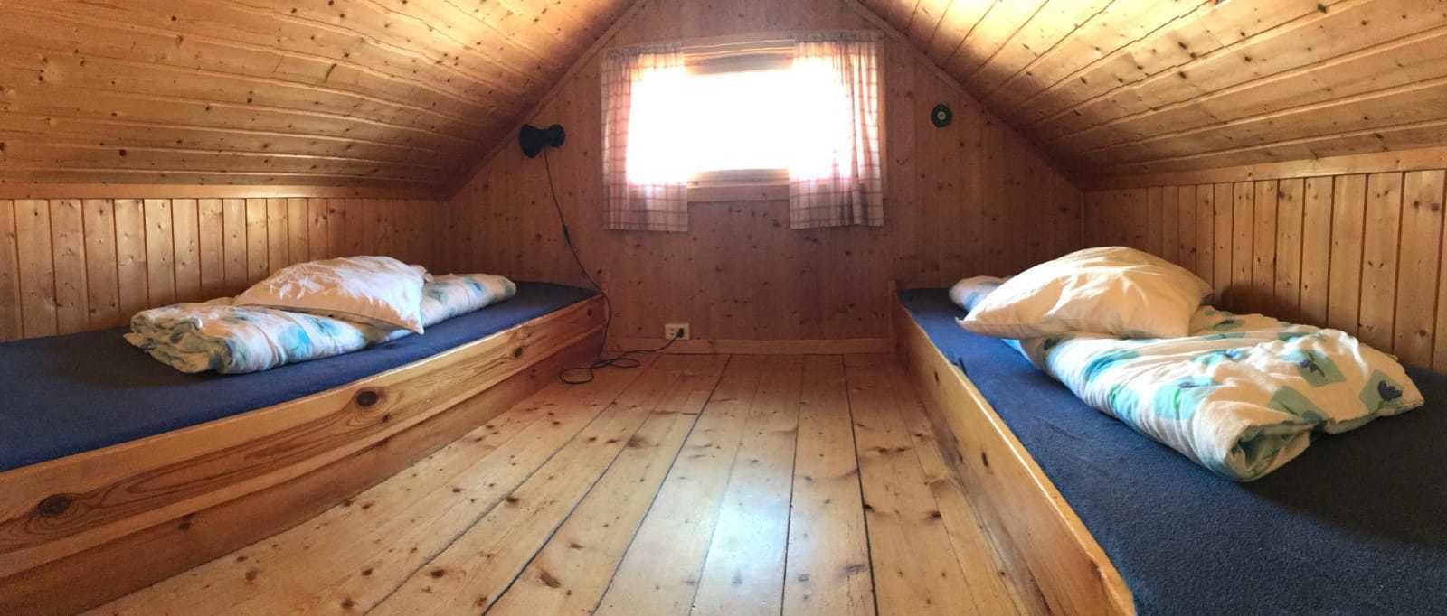 Una petita cabana de fusta amb dos llits superposats, una finestra amb cortines i un paviment de fusta.
