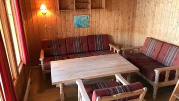 Interior de cabana de madeira com sofá, uma mesa e prateleira na parede.