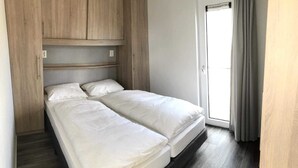 A double bed with a wooden headboard, a small window, and a door leading to a balcony. - O'Lin Lake Resort (Hole)