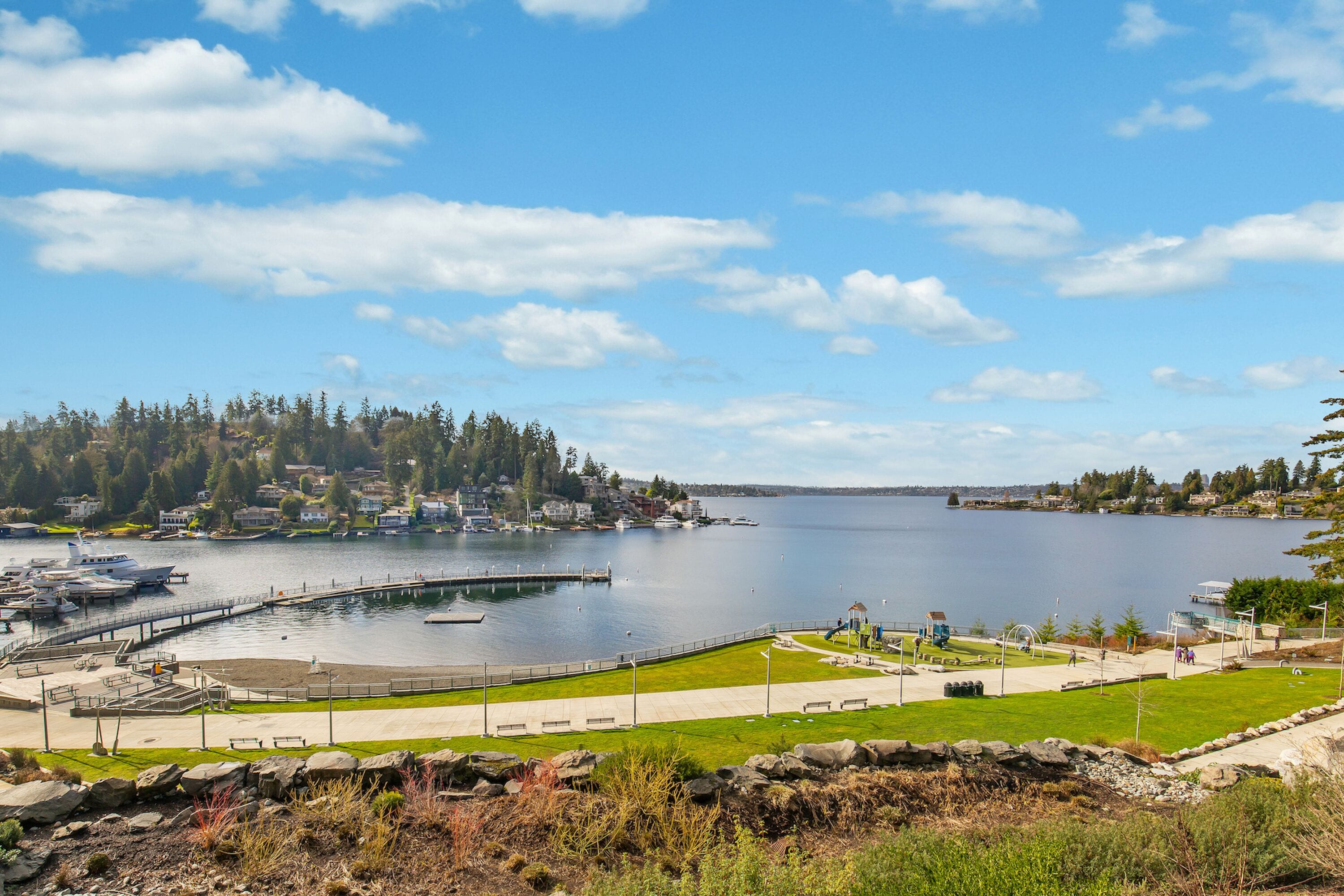 A waterfront park with a marina, walking paths, and a view of a residential area across the water.
