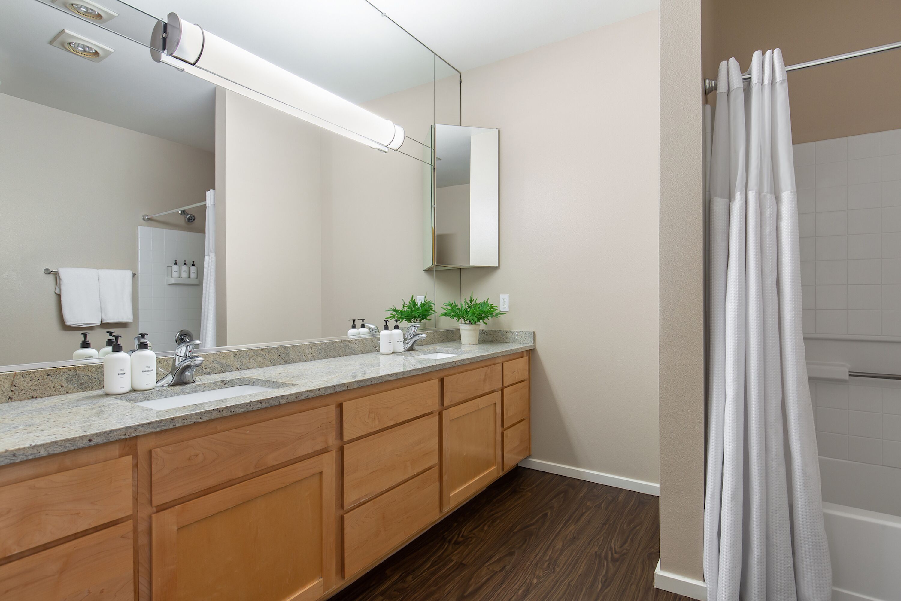 A modern bathroom with a wooden vanity, a large mirror, and a shower with a white curtain.