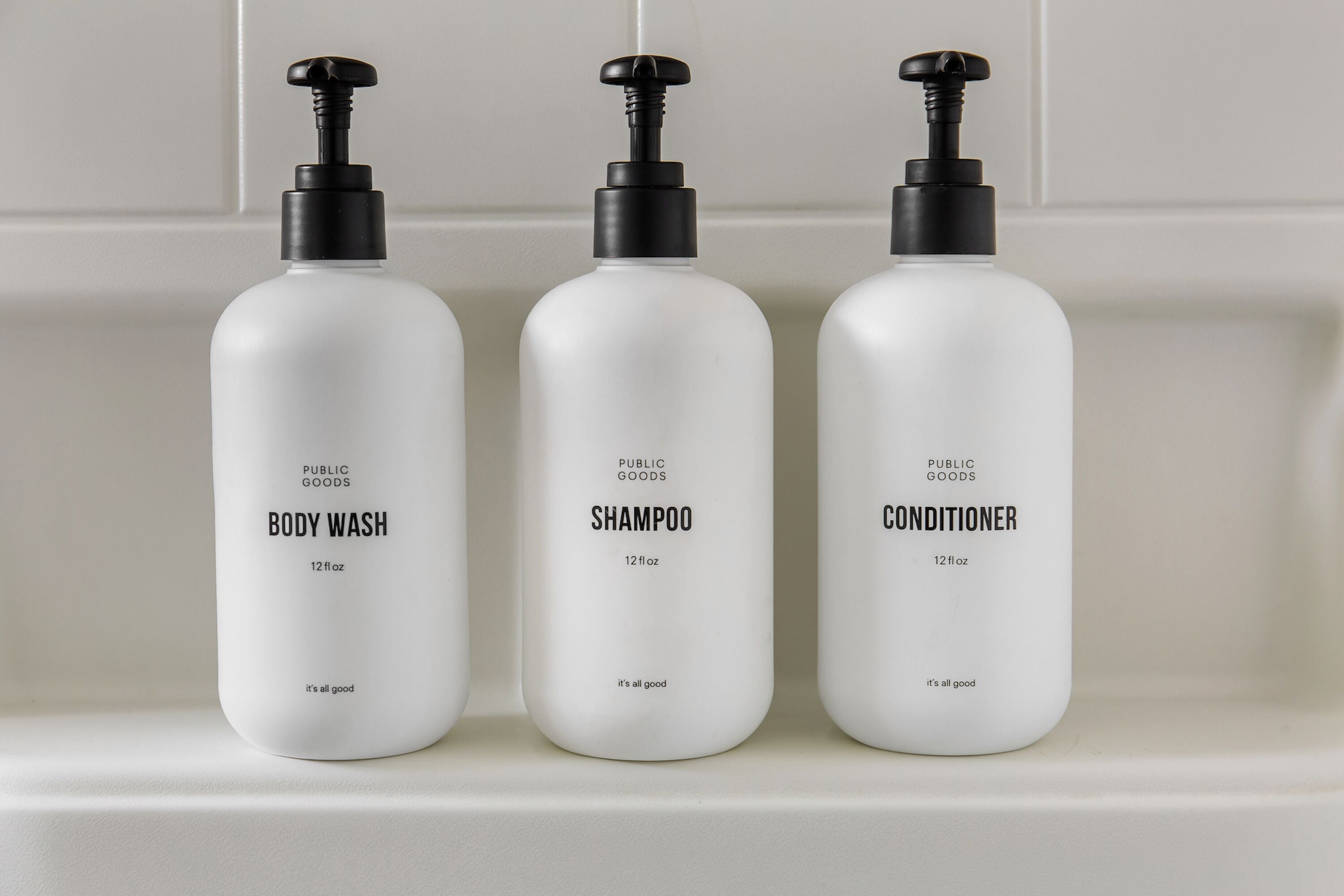 Three white bottles of body wash, shampoo, and conditioner on a shelf.