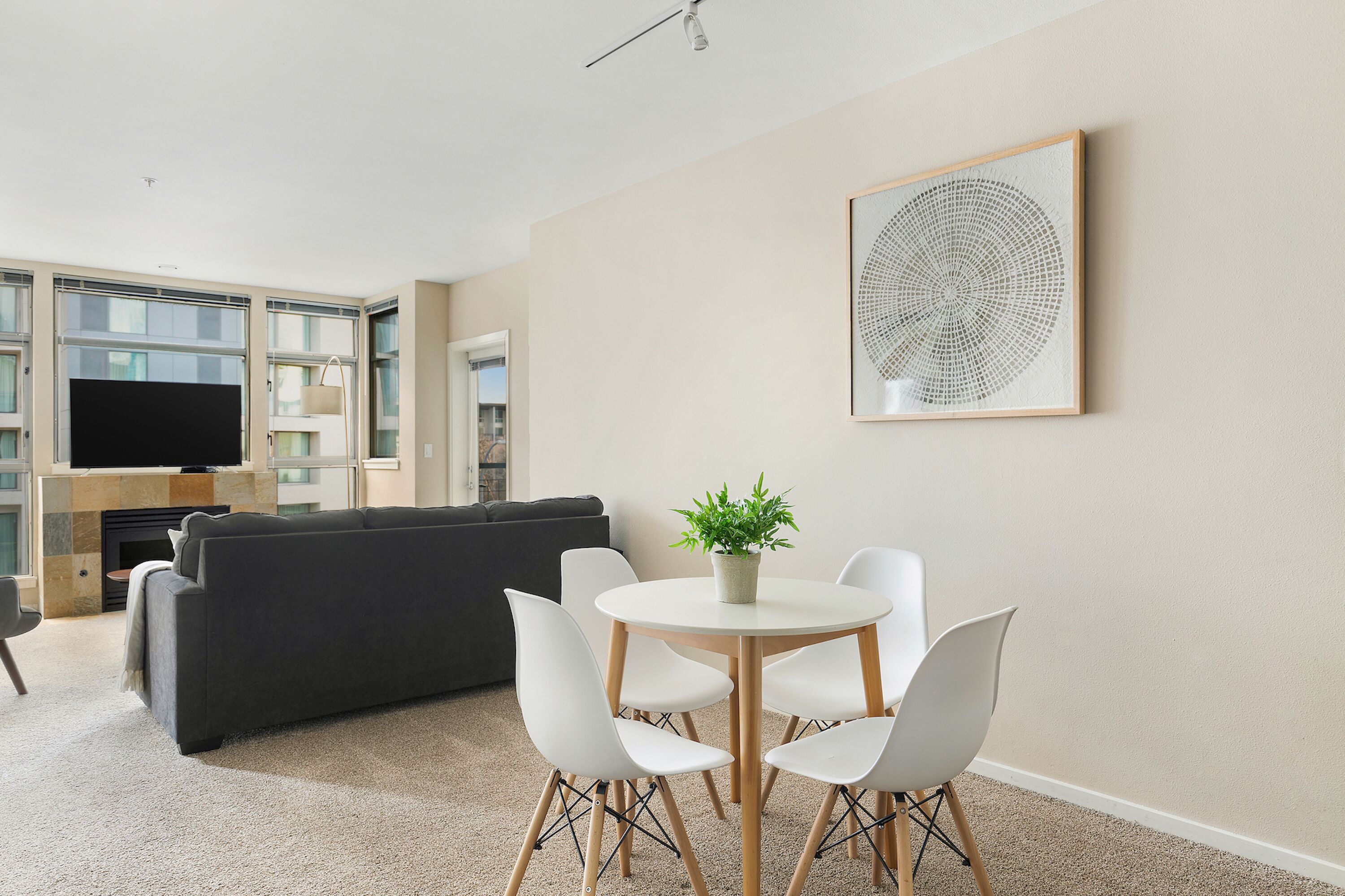 Een moderne woonkamer met een bank, een eettafel met stoelen, een potplant en een groot abstract kunstwerk aan de muur.