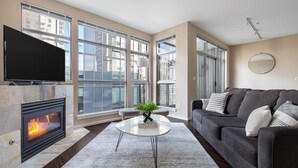 A modern living room with a fireplace, large windows, a grey sofa, and a flat-screen TV. - Kasa Bellevue Seattle (Bellevue)