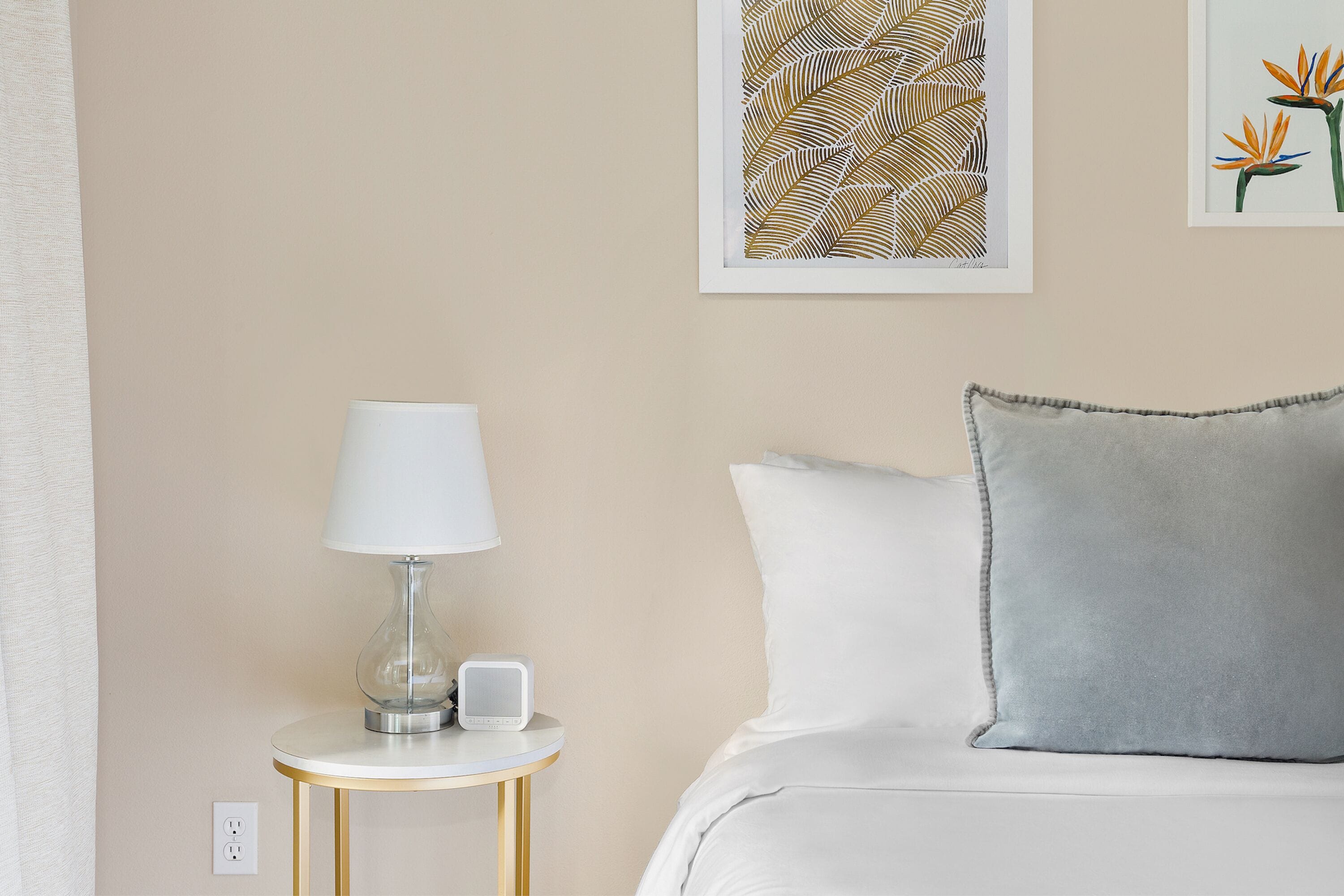 A neatly arranged hotel room with a bed, a bedside table with a lamp, and a wall-mounted power outlet.
