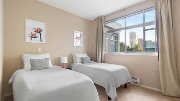 A hotel room with two beds, beige walls, and a large window with a view of buildings.