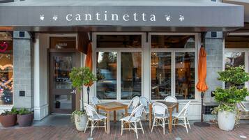 En butik med namnet ”cantinetta” ovanför ingången, med en uteplats med tegelbeläggning, utomhusmöbler och krukväxter.